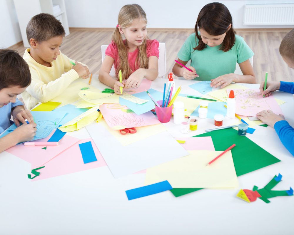 Smart schoolboys and schoolgirls drawing with colorful highlighters in classroom